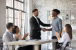 © fizkes - Smiling executive congratulating successful African American employee with promotion, shaking hands at corporate meeting, confident team leader greeting new member at briefing in boardroom