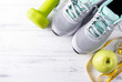  sneakers, green Apple, green dumbbell, measuring tape on a white wooden background top view