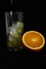 glass of freshly squeezed orange juice with ice on black background