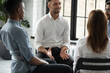 © fizkes - Smiling confident psychologist speaking at group therapy session, young man sharing problems with diverse people sitting in circle, listening to coach at meeting, mentor training staff