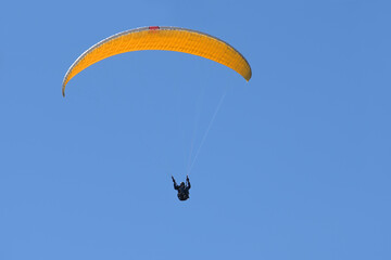 Paraglider pilot with an orange yellow glider is flying in the clear blue sky, recreational and competitive adventure sport, large copy space