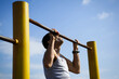 A young man of Caucasian appearance pulls himself up on a horizontal bar. The guy is hanging on one arm. Healthy lifestyle, affordable outdoor sports