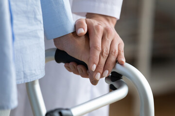 Wall Mural - Physiotherapist touches disabled elderly woman hand while she holding walking frame close up view. Nurse supporting patient during exercise rehabilitation therapy. Caregiving, help, eldercare concept