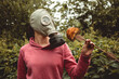 © mynoemy1 - Girl in rubber and metal anti virus and nuclear war and gas mask try to smell artificial wooden flower outdoor, warm tones