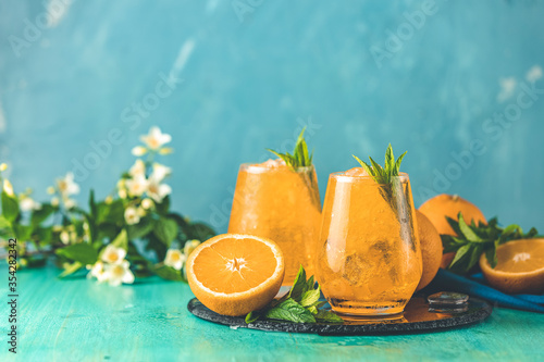 Two glasses of orange ice drink with fresh mint on wooden turquoise table surface. Fresh cocktail drinks with ice fruit and herb decoration. Alcoholic non alcoholic beverage, summer fresh drink