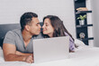 © LIGHTFIELD STUDIOS - bi-racial man and attractive woman with closed eyes near laptop on bed