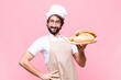 young crazy baker man holding bread against pink wall