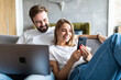 © F8  \ Suport Ukraine - Beautiful young couple relaxing on a couch at home using laptop computer and mobile phone