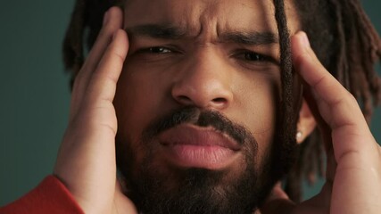 Sticker - A close-up view of a displeased young african american man is touching his temples standing isolated over green wall background in studio