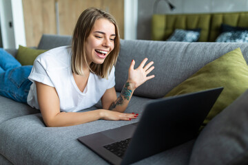 Smiling girl sit on couch at home wave talk with friend or family having video call on laptop. Happy young woman greeting say hello, speak communicate using dating online application on computer