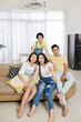 © DragonImages - Group of cheerful friends sitting on sofa at home and smiling at camera