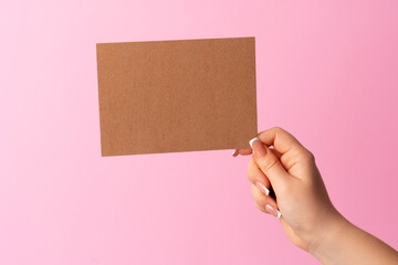 Woman hand showing blank business card on pink background.