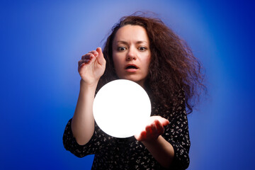 Smiling girl holding a glowing ball in her hands. Blue background.