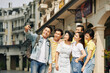 © DragonImages - Happy young Vietnamese man taking selfie with friends when they are walking in historical center of city