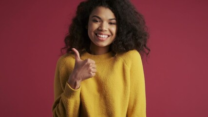 Wall Mural - Young pretty cheerful african woman isolated over dark red burgundy background showing thumbs up gesture