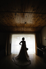 Silhouette of a bride in a wedding dress against the background of a hotel room window.