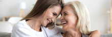 Grown Up Daughter Cuddle Old 60s Mama Happy Excited Women Laughing Seated On Sofa In Living Room. Family Bond, Care And Love Concept. Horizontal Photo Close Up Banner For Website Header Design Concept