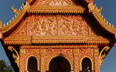 Colorful gable wall flank with golden ornaments and buddha images at a temple site in Siamese Lao PDR, Southeast Asia