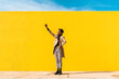 © VISTA by Westend61 - Young man dancing in front of yellow wall, taking selfies