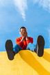 © VISTA by Westend61 - Young man with headphones, sitting on yellow wall, listening music
