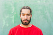 © VISTA by Westend61 - Portrait of bearded young man wearing red sweatshirt in front of green wall