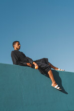 Young Man Wearing Black Kaftan Lying On Blue Wall Holding Oranges