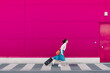 © VISTA by Westend61 - Young woman with smartphone running with trolley along a pink wall