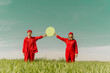 © VISTA by Westend61 - Young couple wearing red overalls  standing on a field holding green circle