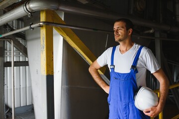 Wall Mural - Smiling and happy employee. Industrial worker indoors in factory. Young technician with white hard hat.