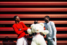 Three Laughing Young Men With Huge Teddy Bear At Red Wall