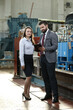 © VItaliy - Portrait of a solid businessman with his secretary holding laptop and tablet, talking about factory financial report in a airplane manufactory.