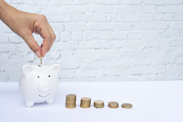 Hand putting money coin piggy bank and money coin stack  on white table. Financial concept, saving concept