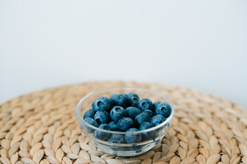 fresh ripe blueberries in a glass bowl on a natural wicker napkin made of dry seaweed on a white background. the concept of healthy food, vegan food