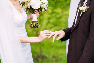 Wedding couple. Bride and fiance at outdoor wedding ceremony. Bride putting golden ring on groom's finger on green grass background. Marriage concept.