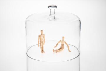 Transparent glass dome with two wooden mannequins within. One standing and the other seated on the ground. They illustrate the lockdown due to an exterior factor.