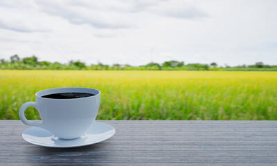 Wall Mural - Black coffee in a white coffee mug and saucer on the table. Wooden floor. The background is a picture of a blurred cornfield and golden brown rice fields. 3D Rendering