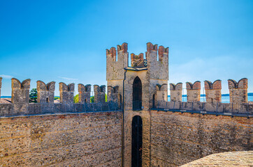 Tower and stone defense wall with swallowtail merlons of Scaligero Castle Castello di Sirmione medieval fortress, Sirmione town on Garda lake, blue sky background, Lombardy, Northern Italy