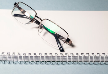 Poster - eyeglasses black on white planner notebook on blue table. Office work concept