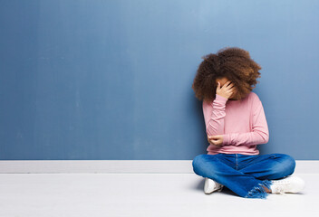 Wall Mural - african american little girl looking stressed, ashamed or upset, with a headache, covering face with hand sitting on the floor