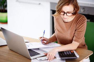 Woman sitting at laptop computer, making notes, calculating expenses, planning family budget, debts and credits, mortgage and rent. Remote working of employee at home, or start up of business woman