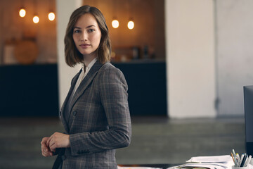 Beautiful portrait of very attractive female CEO business woman wearing a suit standing in her office looking confidently in camera. 