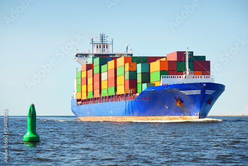 Large cargo container ship sailing from Europoort (Rotterdam, Netherlands) in an open sea on a clear day, navigational buoy close-up. Global communications, logistics, industry theme