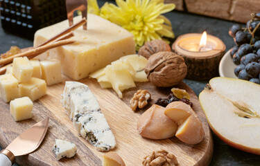 Cheese plate from different kind of cheese - Emmental, Homemade, Parmesan, blue cheese, bread sticks, walnuts, raisin, pear, grapes on a table