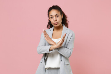 Wall Mural - Serious young african american business woman in grey suit white shirt isolated on pink background studio portrait. Achievement career wealth business concept. Showing stop gesture with crossed hands.