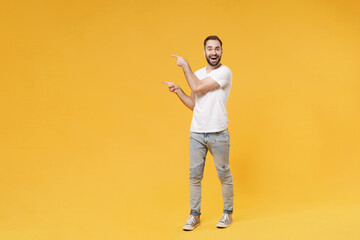 Excited young bearded man guy in white casual t-shirt posing isolated on yellow background studio portrait. People sincere emotions lifestyle concept. Mock up copy space. Pointing index fingers aside.