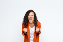 Young Black Woman Shouting Aggressively With Annoyed, Frustrated, Angry Look And Tight Fists, Feeling Furious Against White Wall