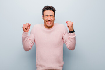 young arabian man looking extremely happy and surprised, celebrating success, shouting and jumping against gray wall