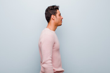 Wall Mural - young arabian man on profile view looking to copy space ahead, thinking, imagining or daydreaming against gray wall