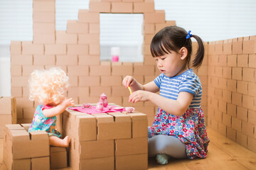 Wall Mural - toddler girl pretend play baby care in a cardboard block house