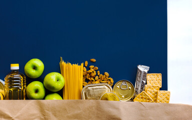 Wall Mural - Food delivery, Donation. Food supplies crisis food stock for quarantine isolation period on blue background. Pasta, canned food, apples, oil, crackers.